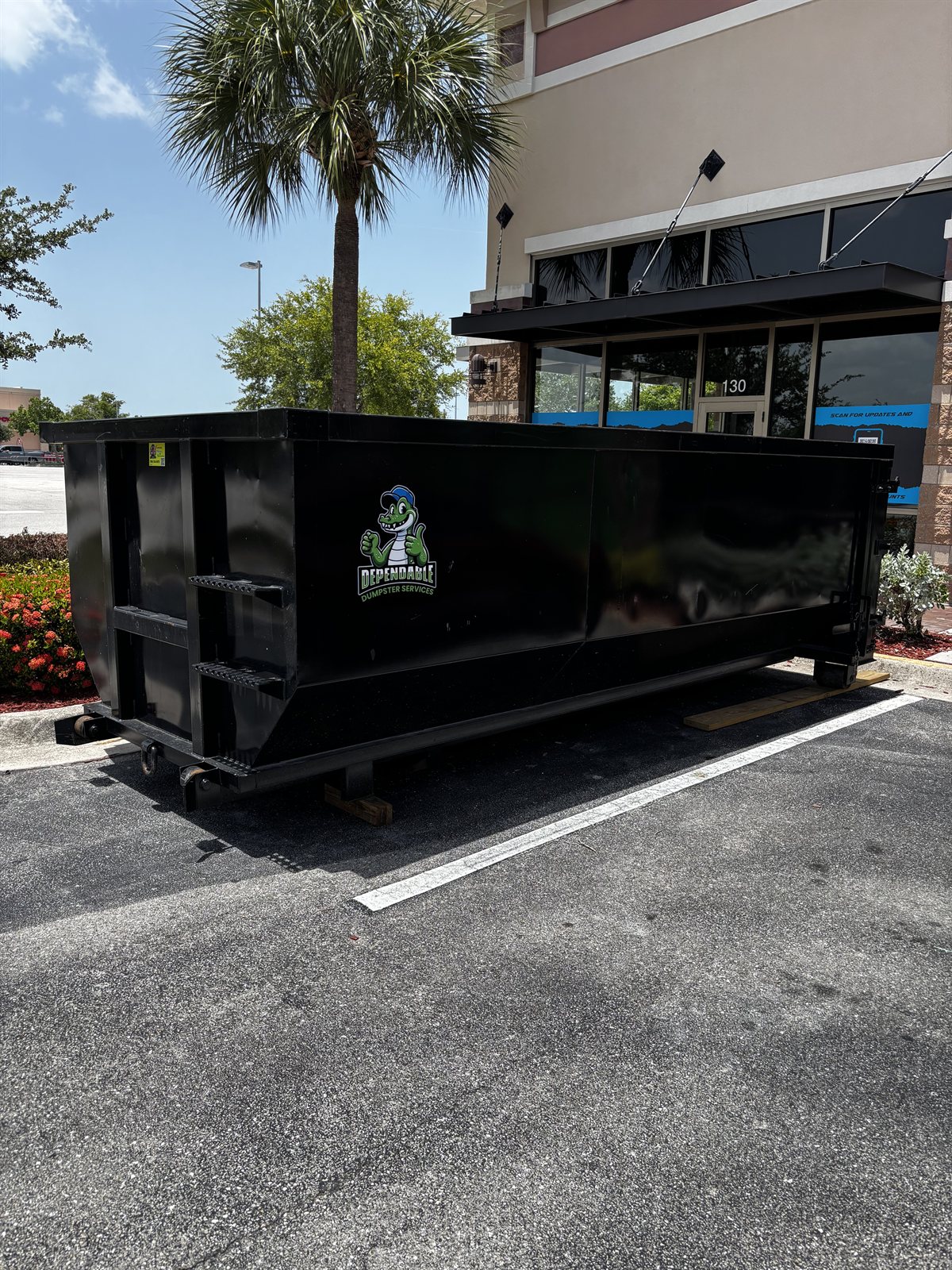 16-foot 20-yard roll-off dumpster at a commercial storefront with a palm tree
