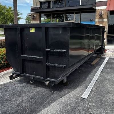 Black 20-yard roll-off dumpster at a Fort Myers commercial storefront